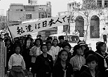 那覇市内で繰り広げられた中高校生たちの「平和を祈る大行進」。「日本復帰」の時期さえまったく見通せないなか、若者たちの心は揺れていた。先頭集団の手には大きな「日の丸」が……。「私達は日本人です」の横断幕を手にした一団もいた。1965年